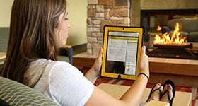 Woman reading resources on a tablet in front of fireplace
